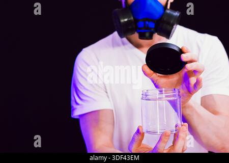 Figure wearing protective gear removes lid from clear container on dark violet-lit background Stock Photo