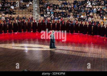 After the end of the Şeb-i Arus ceremony at the Mevlana Kültür Merkezi in Karatay, Konya, Turkey, a venue that holds up to 3,000 people, the dervishes are once again wrapped in their black cloaks, and the Şeyh (sheikh/master) strides towards the exit. Seen from a greater distance, the Şeyh crosses the stage floor in front of the dervishes kneeling in a semicircle. Şeb-i Arus is the annual festival marking the death anniversary (17 December) of the mystic poet Rumi (Jalāl ad-Dīn ar-Rūmī, 1207–1273), founder of the Mevlevi order, celebrated as a spiritual union with God. Stock Photo