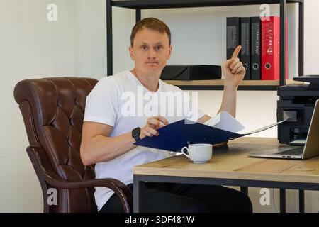 Office worker gesturing idea with finger raised, examining papers in blue binder at modern desk setup Stock Photo