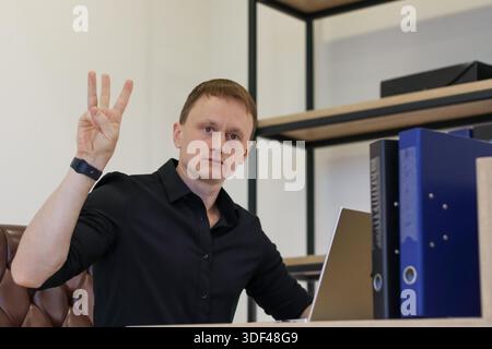 Office worker showing three fingers gesture at desk with computer and document holders Stock Photo