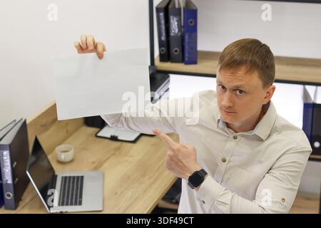 Businessman in office pointing to held blank sheet, ideal for advertising or instructional use Stock Photo