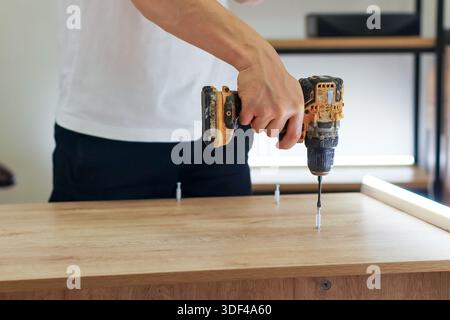 Male figure in casual attire using power drill on wooden tabletop with aligned fasteners Stock Photo