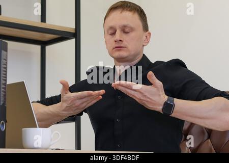 Adult male at desk with electronic device and drink, displaying upward palm position with thoughtful expression in professional environment. Stock Photo