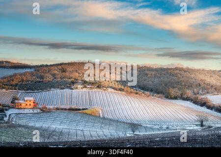 Breathtaking winter sunset over snowy vineyards and a stone farmhouses near Radda in Chianti. Rare snow-covered Tuscan landscape in Italy. Stock Photo