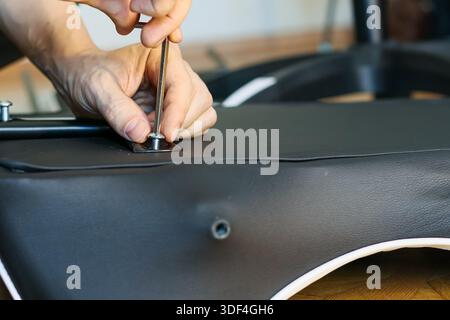Close-up capturing hands with screwdriver securing a bolt on leather chair seat in furniture assembly Stock Photo