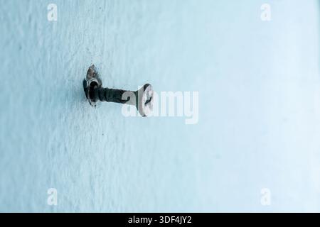 Macro photography of a single weathered screw stuck in a textured pale blue wall, featuring minimalist composition and negative space. Stock Photo