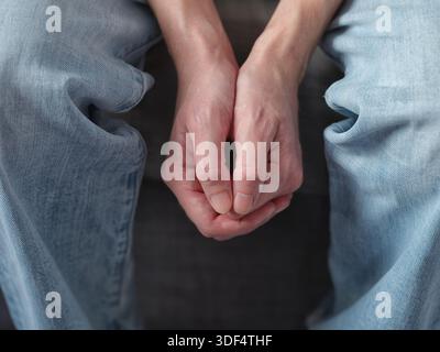 A man clasping his hands together in his lap, conveying emotions of anxiety, stress, or contemplation. Close up. Stock Photo