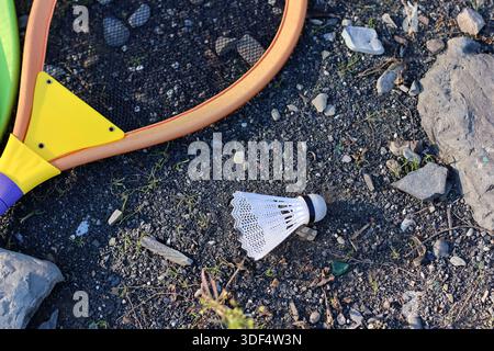 Close-up of orange racket with yellow guard and white shuttlecock on rocky outdoor surface Stock Photo