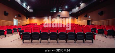 Low-key wide-angle shot of an empty modern cinema auditorium with rows of red plush seats, wide angle symmetrical view from front, warm wood walls, ce Stock Photo