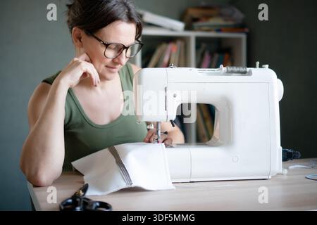 Close up portrait of a concentrated and engaged female seamstress working at her sewing machine in her personal workshop studio. Stock Photo