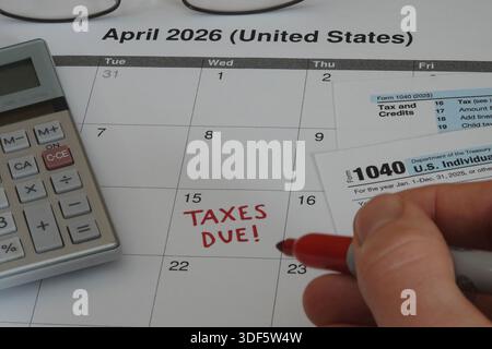 TAXES DUE! is shown written on a calendar by hand, with a form 1040, calculator, and eyeglasses nearby in 2026 for tax year 2025 filing. Stock Photo