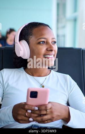 African woman with headphones using smartphone at airport lounge Stock Photo