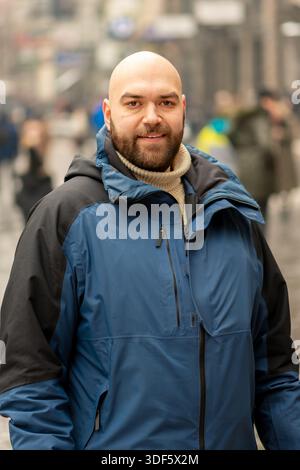 A middle-aged man looks at the camera among the city passers-by Stock Photo