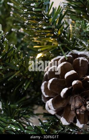 Close-up of a pine cone among green fir branches with soft holiday lights. Natural Christmas decoration, cozy winter mood, festive seasonal background Stock Photo
