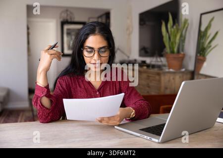 Focused young Indian woman in glasses reading paper letter Stock Photo