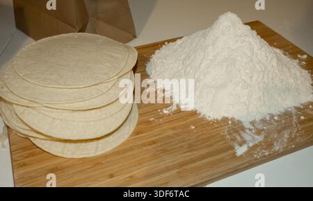 There is a pile of flour on the board and a stack of taco shells next to it. Stock Photo