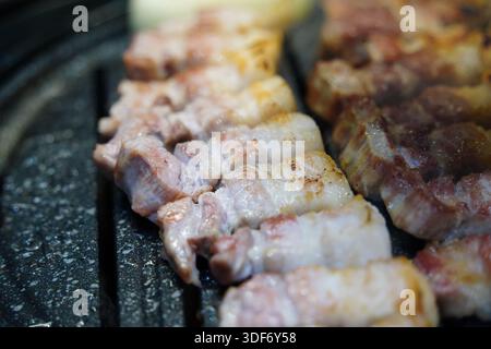 Sizzling Korean pork belly (samgyeopsal) grilling on a hot barbecue, close-up shot. Stock Photo