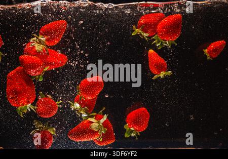 High speed capture of ripe red strawberries suspended in water with dynamic splashes against a dark background. This image conveys freshness, vitality Stock Photo