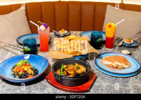 Gourmet meal setup in modern restaurant, featuring seafood pasta, fried dish, desserts, and cocktails. Elegant dining setting for foodies, gastronomy Stock Photo