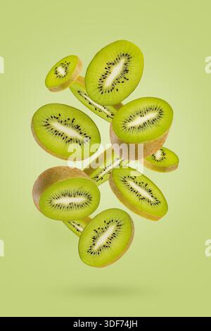 Freshly cut kiwi fruit slices with bright green flesh, tiny black seeds soar as flow on green background. Great for summer detox menu, vitamin product Stock Photo