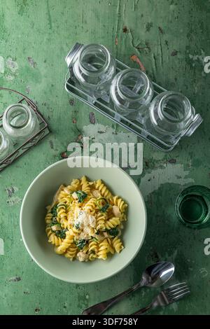 Pasta with chicken and spinach serving in a bowl on a green rustic table Stock Photo