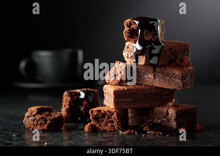 Brownie pieces on a black background. Melted chocolate drips down the brownie. Copy space. Stock Photo