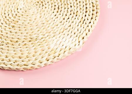 Top view of brown wicker table mat on pink background. Straw round tray, flat lay, copy space. Stock Photo