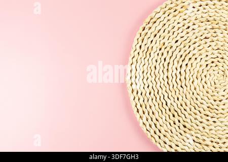 Top view of brown wicker table mat on pink background. Straw round tray, flat lay, copy space. Stock Photo
