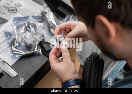 Close-up of a man carefully examining small black electronic parts inside a clear plastic bag for installation or integration into a new device Stock Photo
