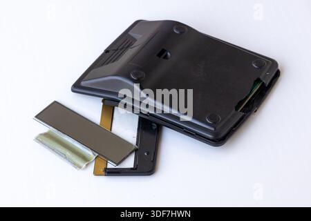 Close-up of a broken black calculator with a detached screen and shattered internal parts scattered on a white background. Concept of financial failur Stock Photo