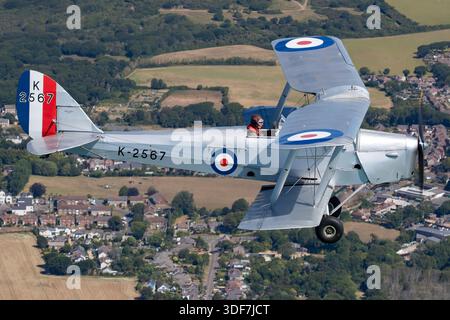 The De Havilland D.H. 82A Tiger Moth II, registration G-MOTH, serial 85340, alternate K2567, is a historic British biplane in Royal Air Force display paint. Powered by a de Havilland Gipsy Major engine, it has tandem open cockpits, dual flight controls, fabric-covered wooden wings, and fixed landing gear. Shown in close-up pilot view air-to-air at UK Warbirds 2025, the aircraft demonstrates classic biplane handling, pilot training configuration, and RAF heritage from the mid-20th century. Stock Photo