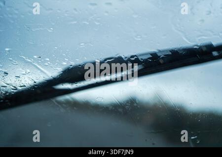Close-up of a windshield wiper blade clearing rain droplets on a car window during a storm. Concept of road safety, driving and rainy weather. Stock Photo