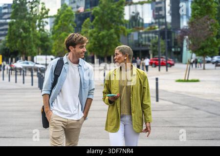 Diverse business colleagues walking outdoors through a modern city park, having an engaging conversation while discussing ideas and collaborating on t Stock Photo