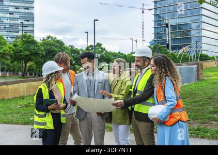 Group of multi ethnic architects, engineers, and executives reviewing blueprints and discussing plans for a new city development, symbolizing teamwork Stock Photo