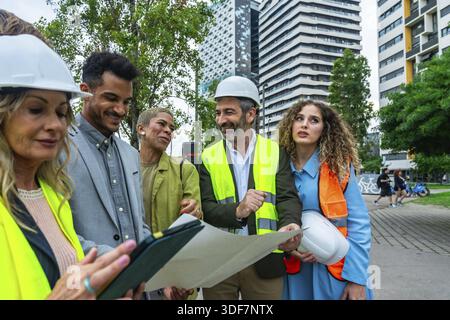 Group of diverse architects, engineers, and real estate professionals collaborating on a building project, discussing plans and digital documents outd Stock Photo