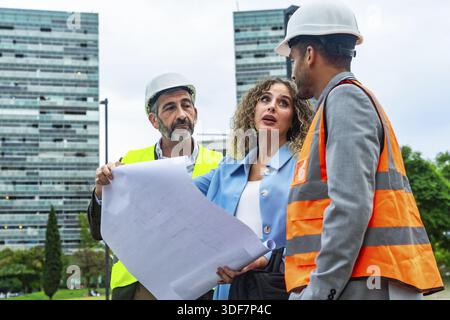 Three construction professionals, including an architect and an engineer, reviewing building blueprints and discussing an urban development project on Stock Photo