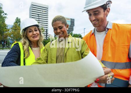 Diverse team of architects and construction professionals collaborating and discussing building plans, ensuring safety and progress in an urban constr Stock Photo