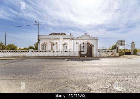 Old traditional house with wooden gate and whitewashed walls in Luz de Tavira, Algarve, Portugal, under a bright blue sky Stock Photo