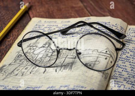 Reading glasses on a vintage travel journal with handwriting and pencil sketches (property release attached) on a rustic wooden table Stock Photo