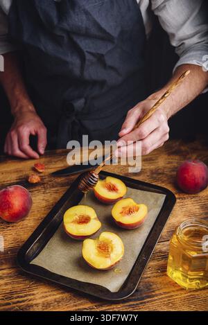Prepare for baking halves of ripe peaches with honey. Chef pour honey over fruits Stock Photo