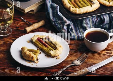Sliced rhubarb mini galette on white plate with glass of white wine and cup of coffee Stock Photo