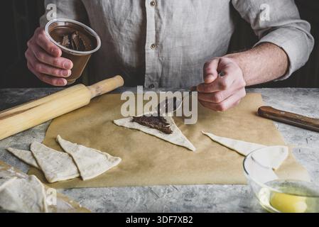 Homemade croissant preparing. Baker distributes hazelnut spread among puff pastry triangles Stock Photo