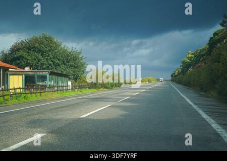 Sunlight breaks through heavy storm clouds over the wet VOAK highway from Rethymno to Heraklion. A lone truck drives on the glistening asphalt Stock Photo