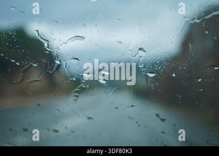 Raindrops on a car window with a blurred rocky background. Moody abstract texture of water droplets on glass. Artistic season rainy concept. Stock Photo