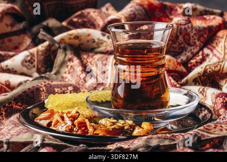 Black tea in armudu glass with candies with different nuts and crystal sugar on metal tray over tablecloth Stock Photo