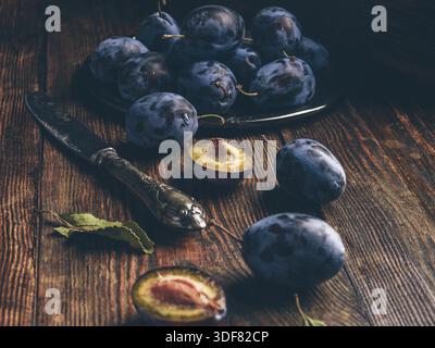 Ripe plums on wooden table with leaves and vintage knife Stock Photo