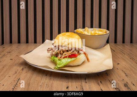 Gourmet burger with a soft pretzel bun, pulled pork, and beer sauce, served with a side of spiral-cut fries arranged in a crispy, golden nest. Stock Photo