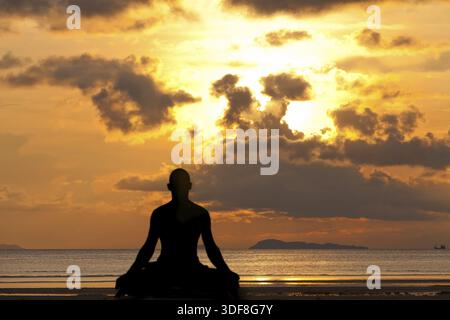 Man silhouette doing yoga exercise at sunset beach Stock Photo