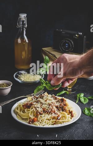 Spaghetti with bolognese sauce and grated parmesan cheese. Hand garnish ready meal with basil leafs Stock Photo