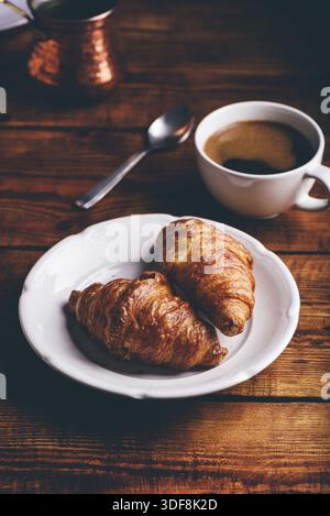 Two Croissants on White Plate and Cup of Black Coffee for Breakfast Stock Photo